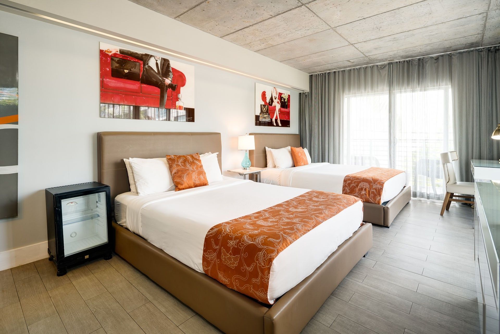 A hotel room with two beds, a mini fridge, and a window with curtains.
