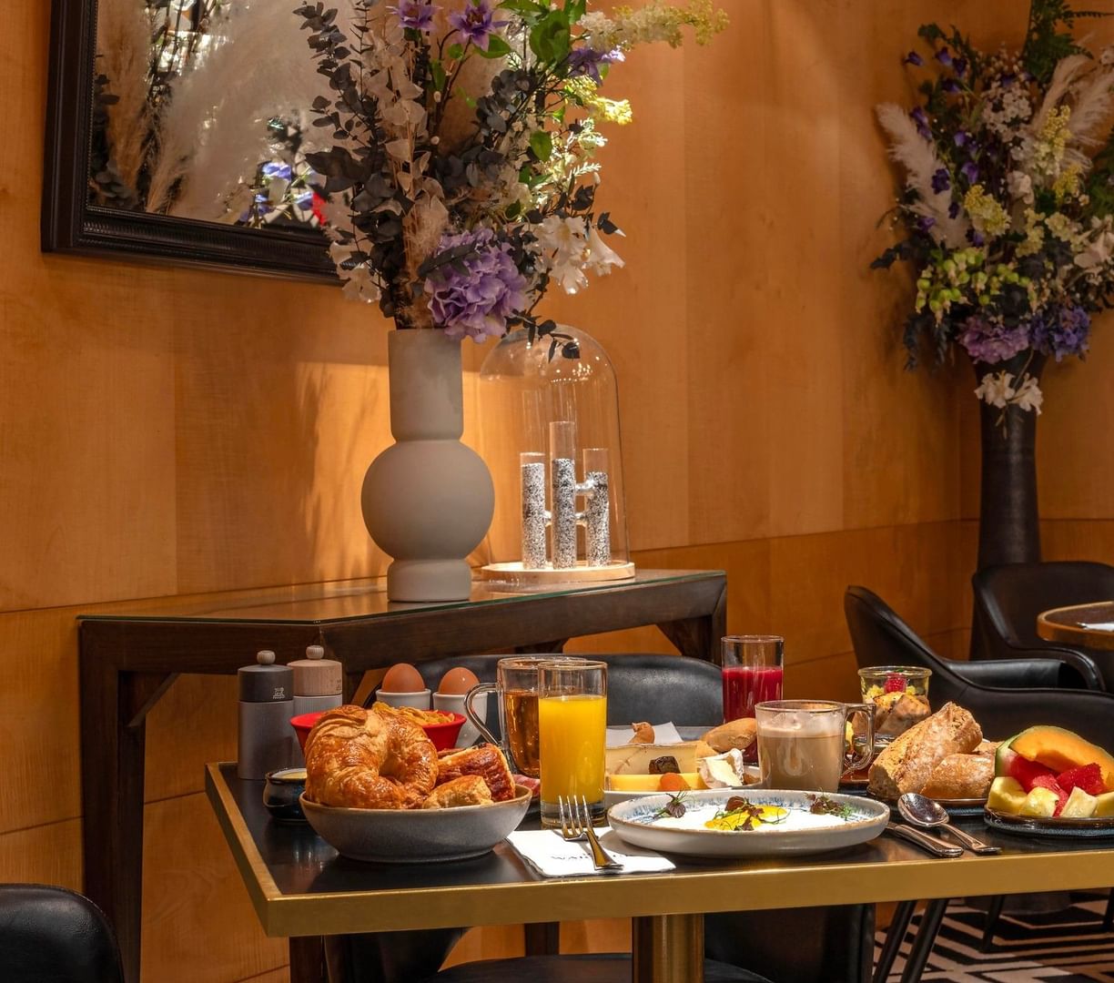 Breakfast table with croissants & fruit by tall flower vases under wood-paneled walls at Restaurant, Bar & Terrace Le W
