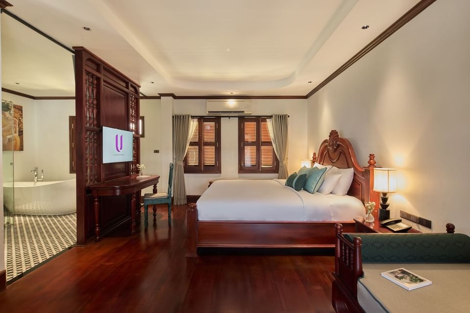 Wooden king bed facing a TV partition near an open bathroom in a luxury room at U Luang Prabang 