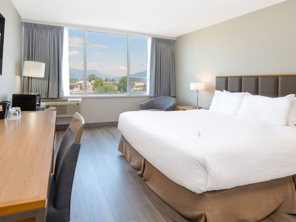 Hotel room with large king bed, desk, chairs, TV and large window with city view.