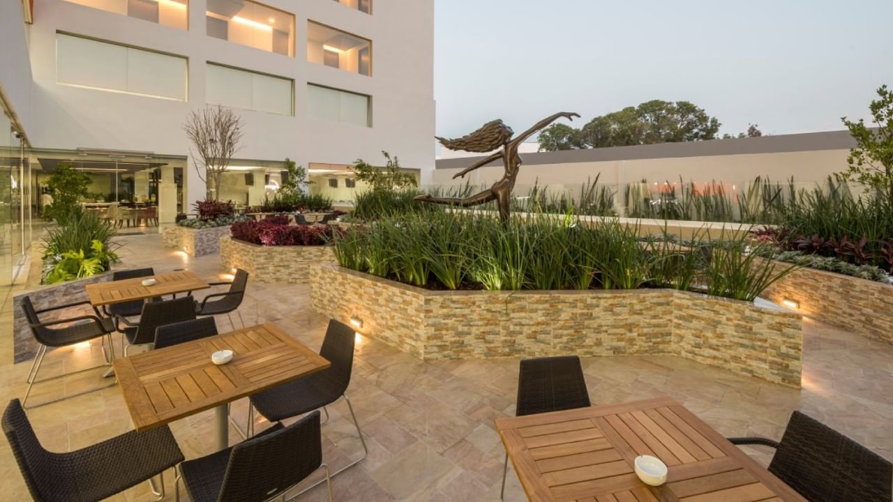 Temple del Carmen with wooden tables, black chairs, a stone planter with lush greenery near Real Inn Celaya