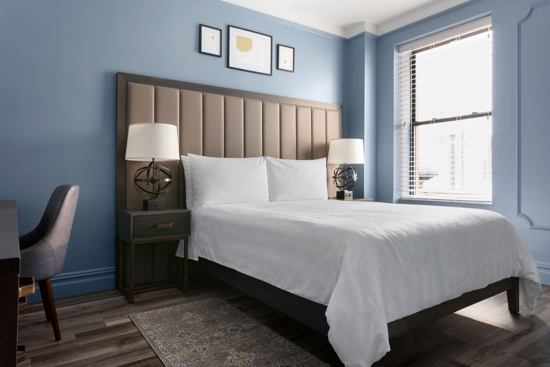 A hotel room with a large bed, a window, a desk, and a chair.