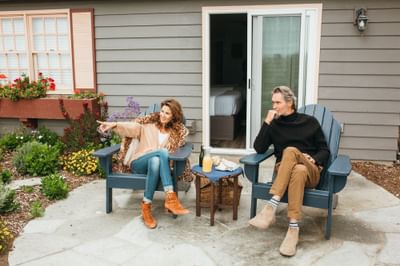 Two people sit on blue chairs on a patio, with a table and garden in the background.