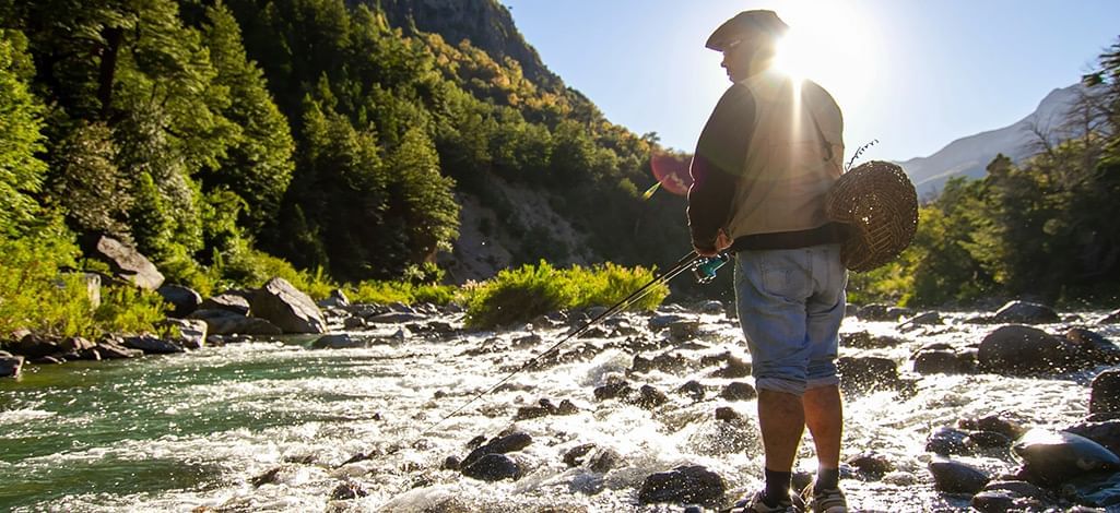 A person fishes in a river in Canmore on a sunny day.