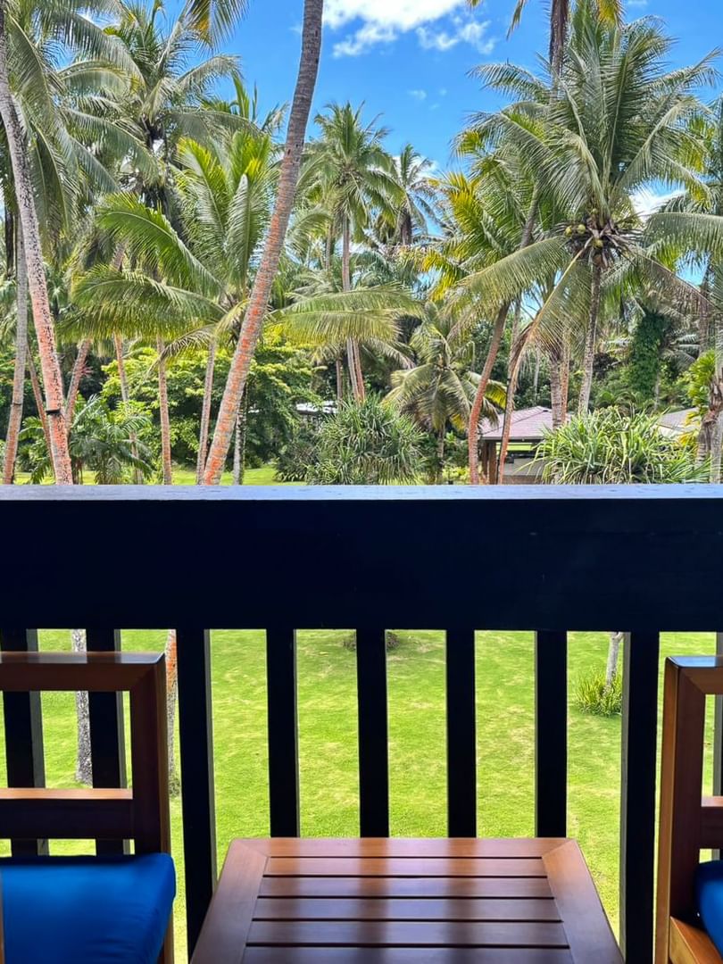 Wooden balcony with chairs and table overlooking lush greenery and palm trees at Warwick Fiji Resort and Spa, Korolevu.