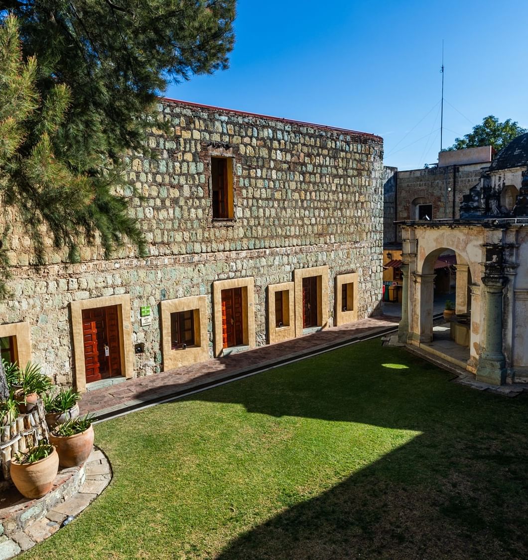 Antiguos edificios de piedra rodeando césped verde en patio soleado en Quinta Real Oaxaca
