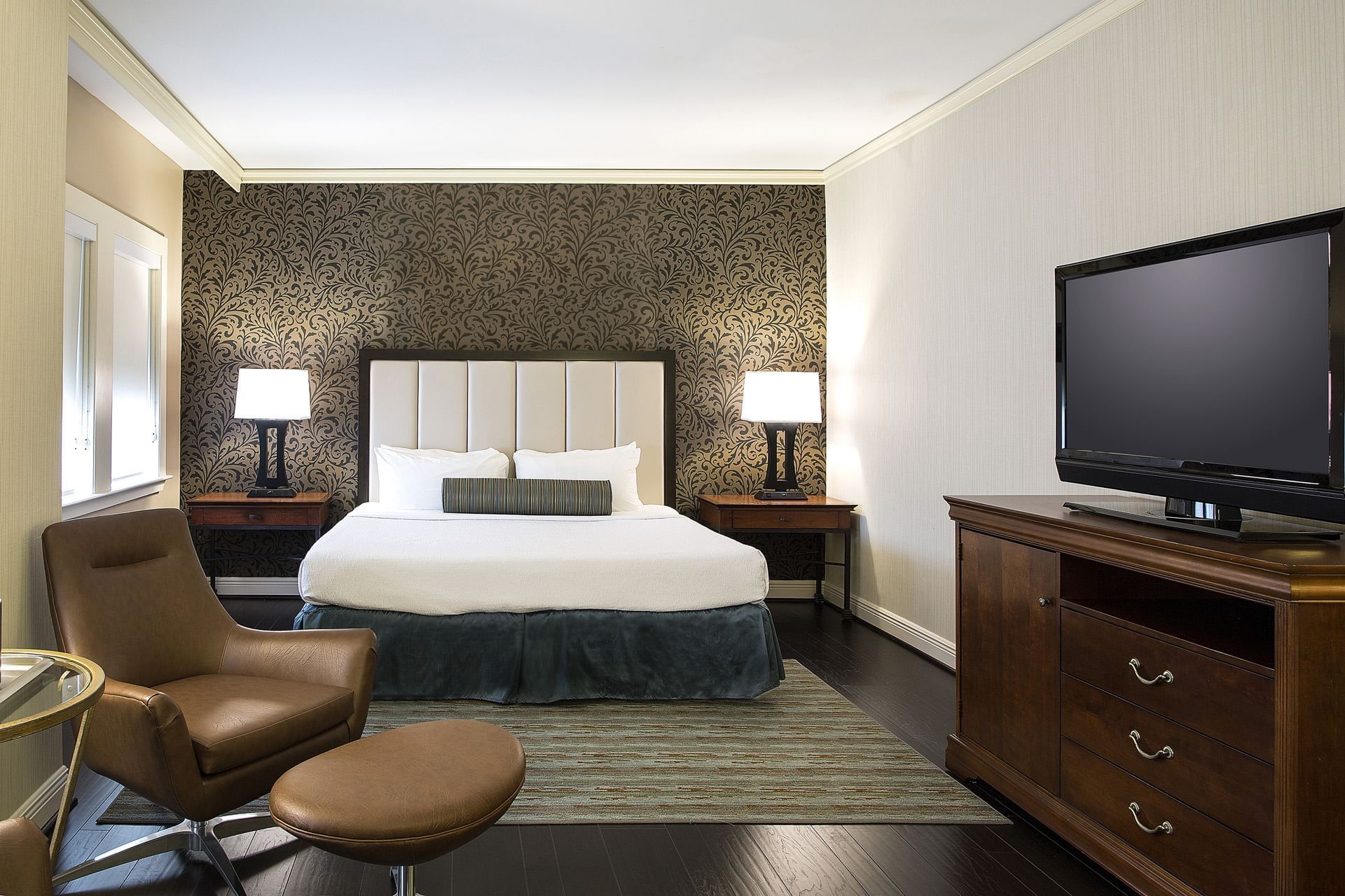 A wide view of a hotel room with a bed, TV, chair, and dresser.