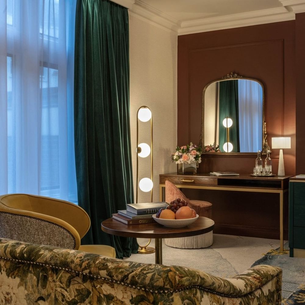 Elegantly furnished Deluxe Room with floral couch, books, & fruit at The Capital Hotel, Apartments & Townhouse, London