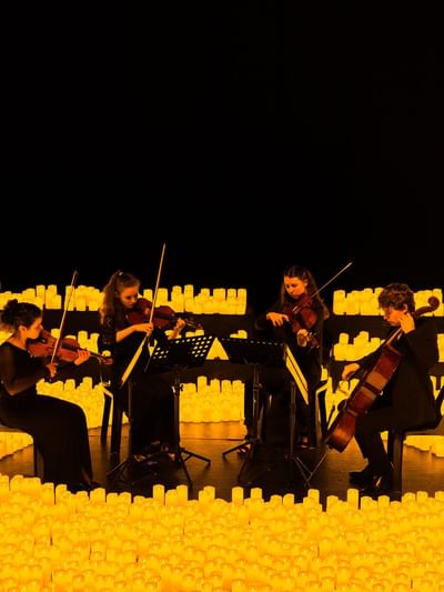 String quartet performing surrounded by glowing candles in a dramatic illuminated setting for La Fête de la Musique