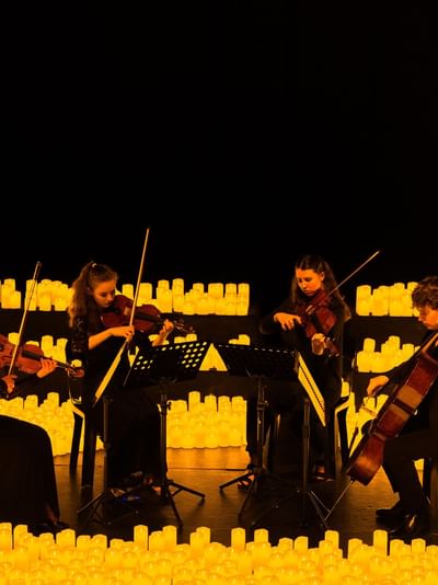 String quartet performing surrounded by glowing candles in a dramatic illuminated setting for La Fête de la Musique