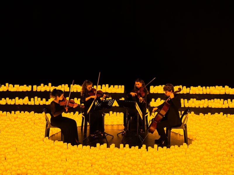 String quartet performing surrounded by glowing candles in a dramatic illuminated setting for La Fête de la Musique