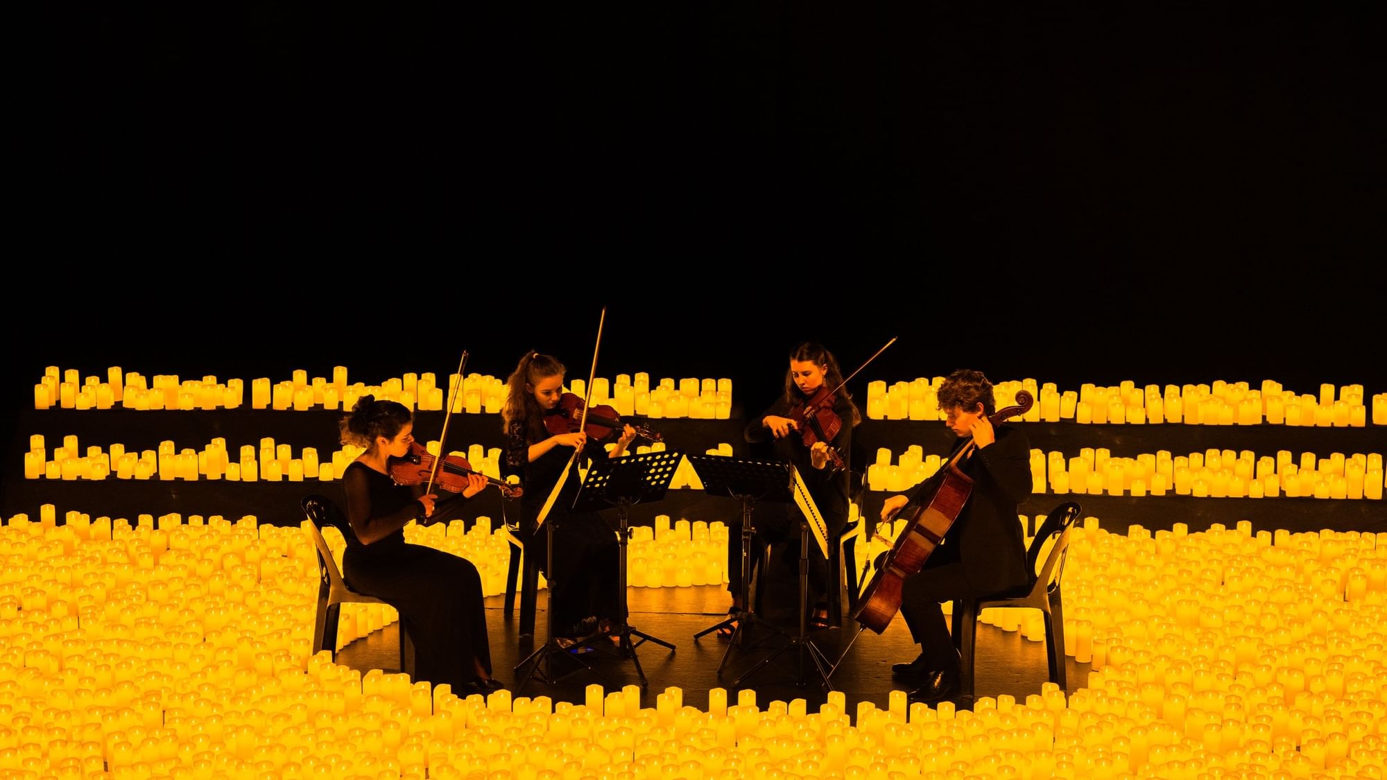 String quartet performing surrounded by glowing candles in a dramatic illuminated setting for La Fête de la Musique