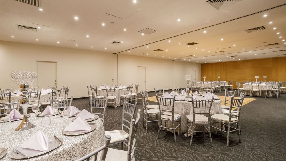 Milan banquet hall featuring round tables with silver chairs and a small wooden dance floor at Real Inn Torreon