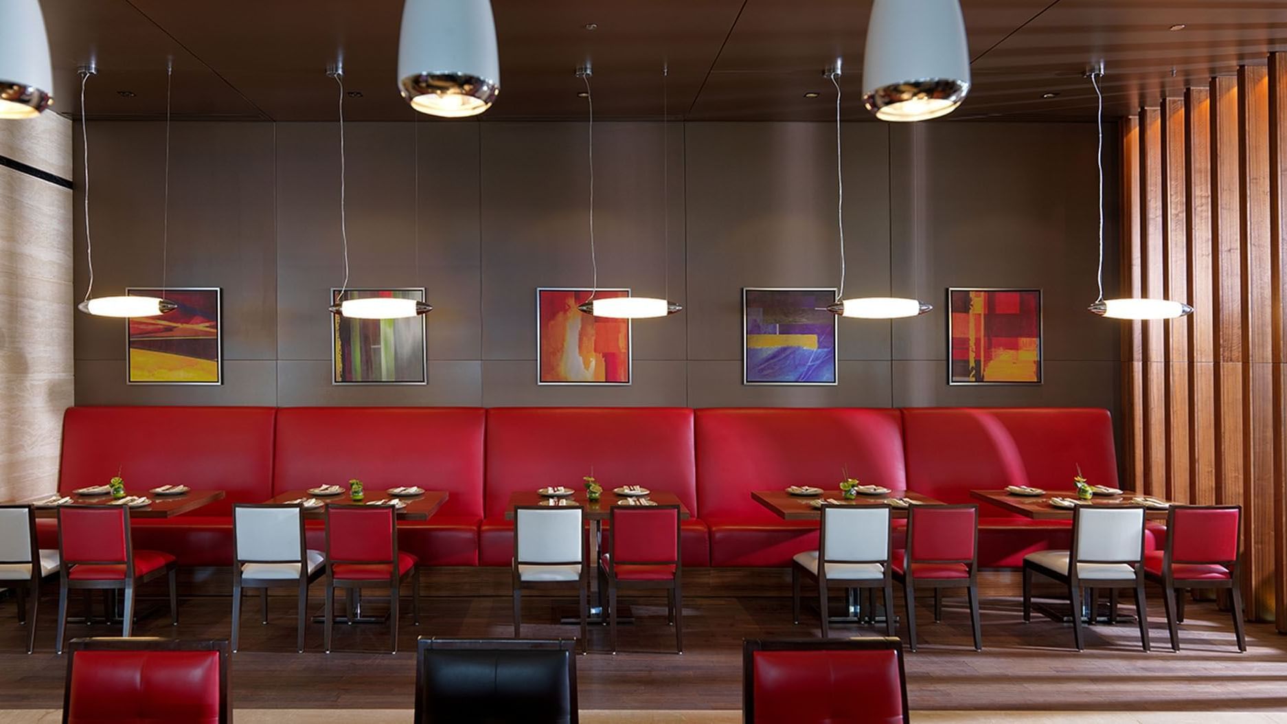 Modern interior with red booths, abstract art, and hanging lights in Maison Cafe, breakfast business bay at DAMAC Maison Cour Jardin