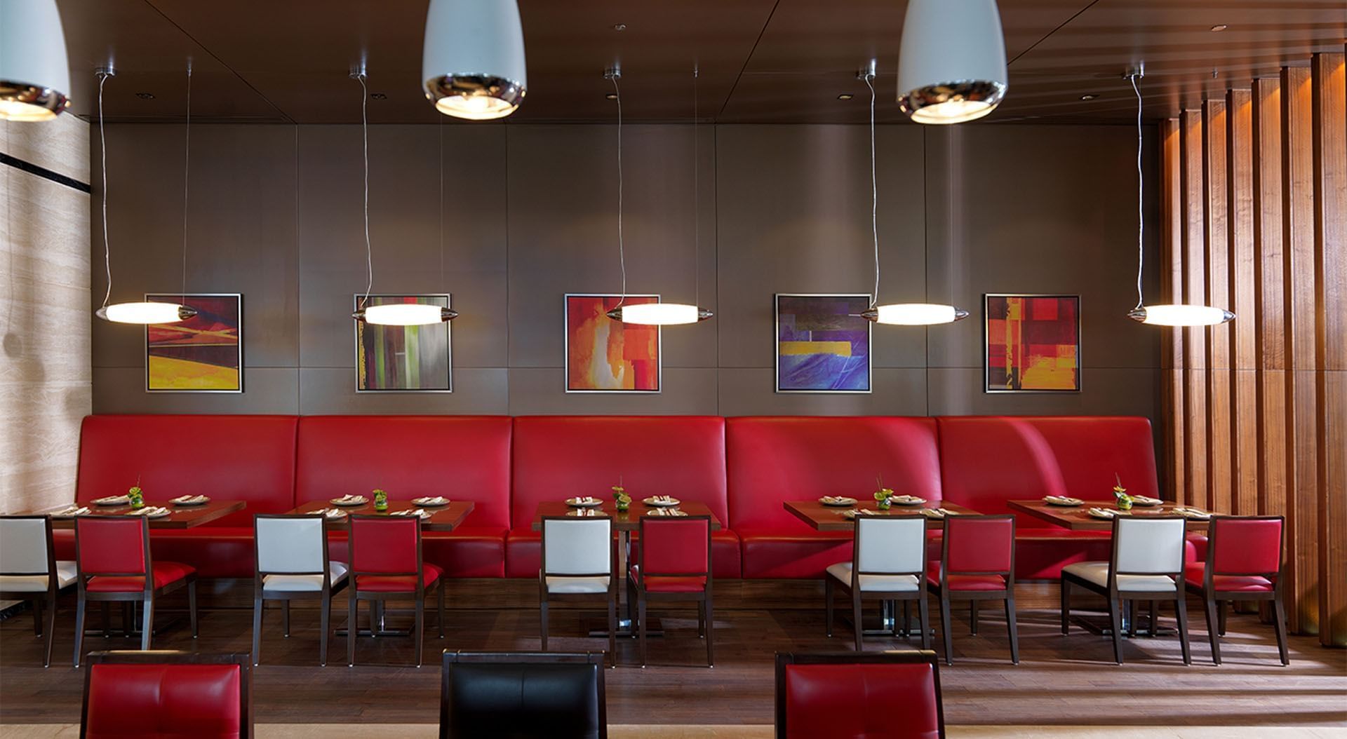 Modern interior with red booths, abstract art, and hanging lights in Maison Cafe, breakfast business bay at DAMAC Maison Cour Jardin