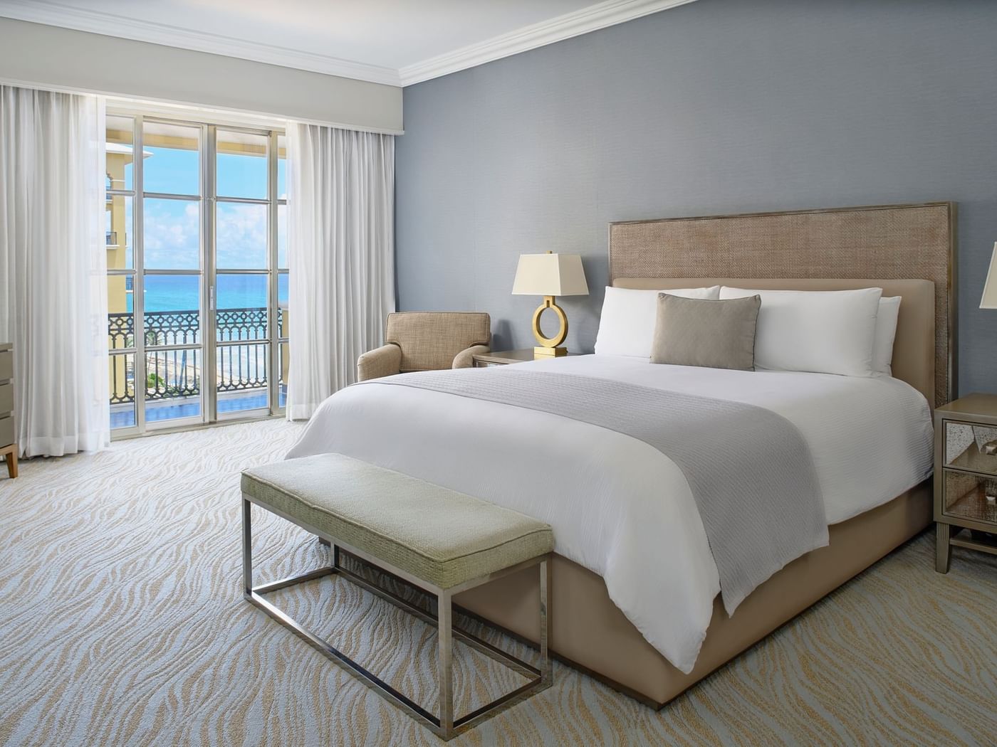 King bed with bench & lounge chair in Seaside Suite with carpeted floors at Kempinski Hotel Cancún