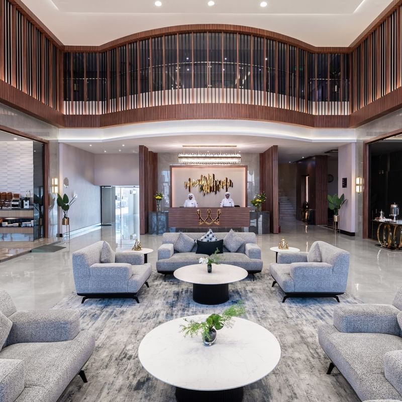 Warwick Al Jubail Hotel lobby featuring plush gray sofas, round marble tables, and a reception area with staff