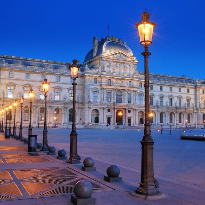 Louvre courtyard with glowing street lamps placed by a stone pathway under a clear twilight sky near Hotel Westminster Paris
