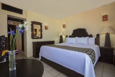 Hotel room with white bedding, dark wood furniture, and purple iris flowers at Playa Los Arcos Puerto Vallarta