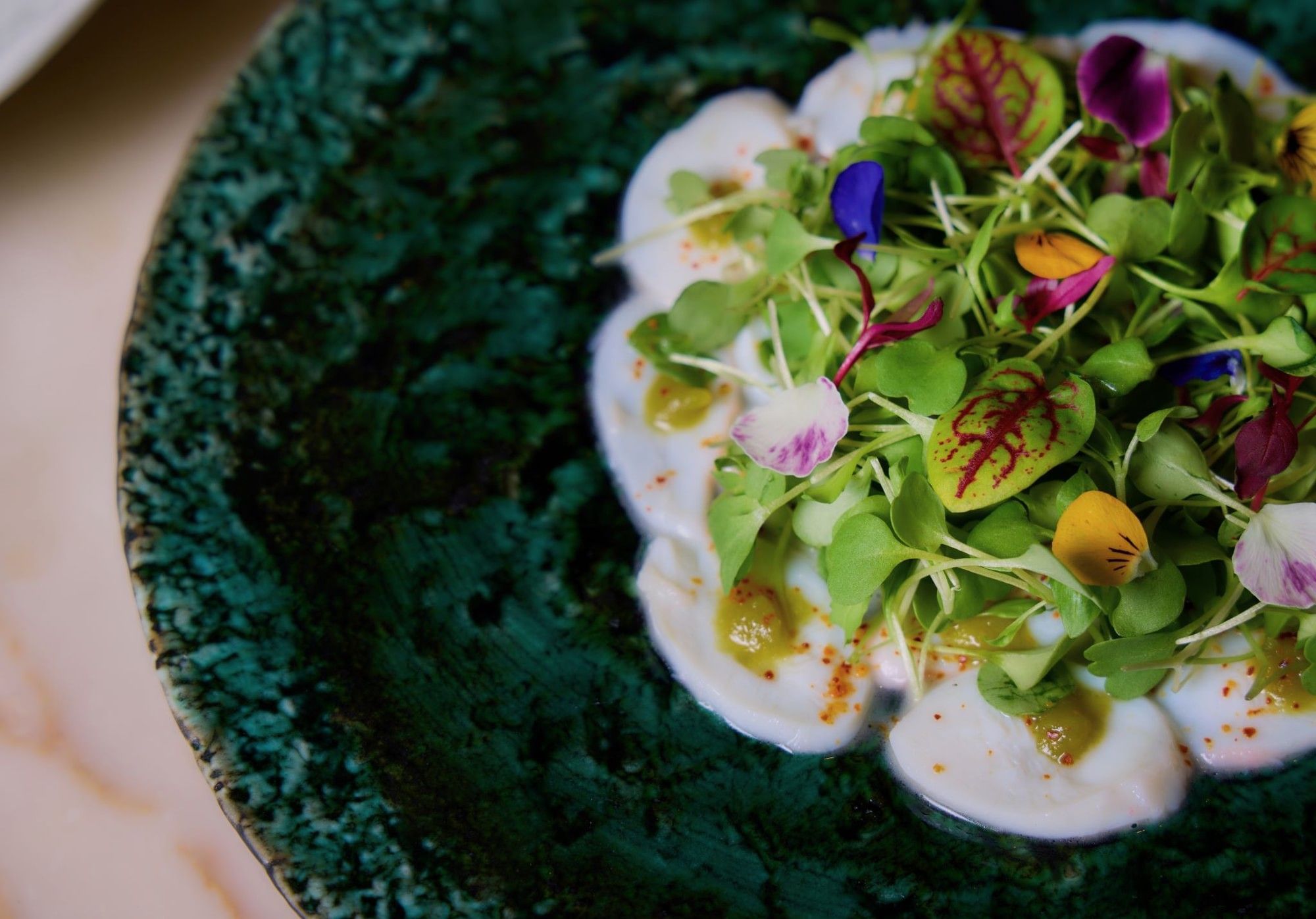 Plate of creamy scallops with greens and colorful edible flowers on a green plate.