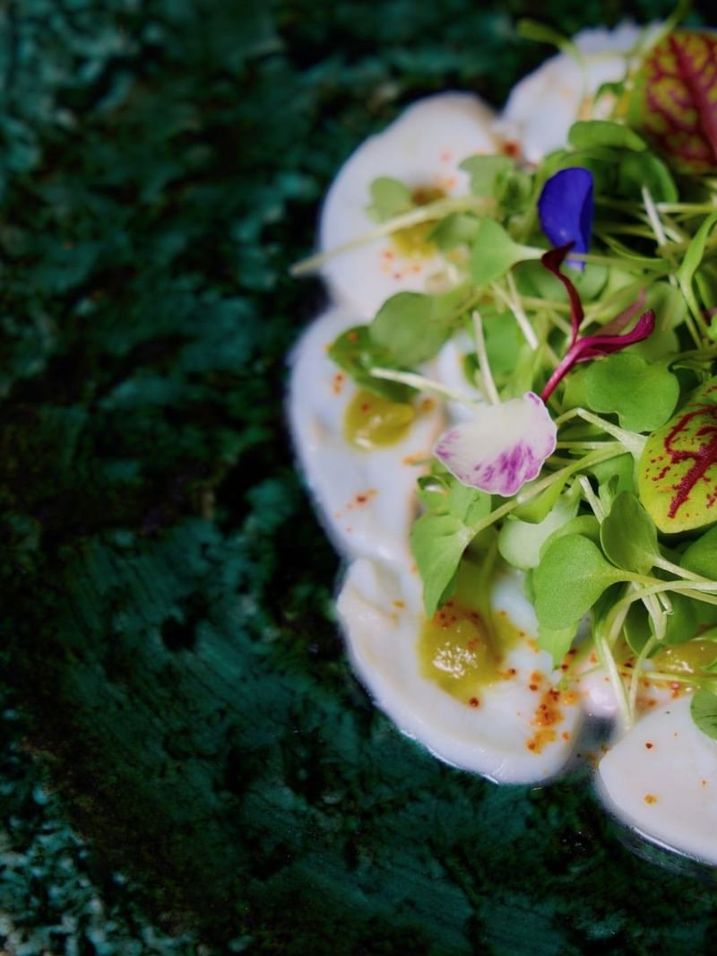 Plate of creamy scallops with greens and colorful edible flowers on a green plate.
