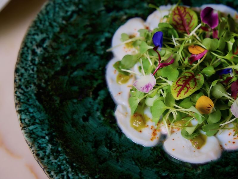 Plate of creamy scallops with greens and colorful edible flowers on a green plate.