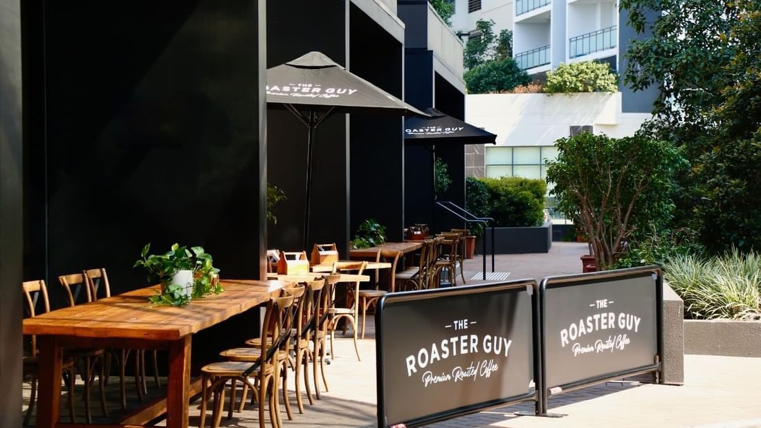 The Roaster Guy cafe’s terrace with outdoor tables and umbrellas at Novotel Sydney International Airport