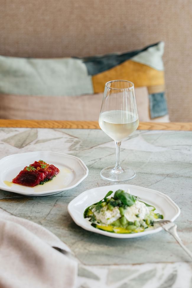 Gourmet dining at Elysium Hotels showcasing fresh tuna carpaccio burrata salad and a glass of white wine on marble table