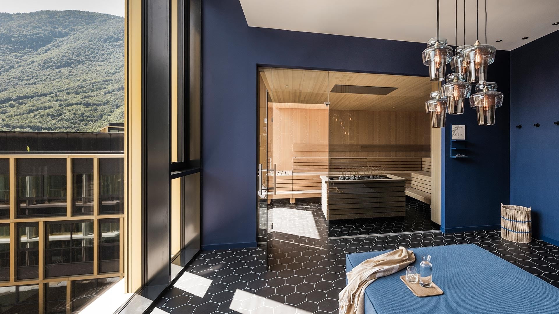 Blauer Raum mit Sauna, schwarz-weißem Boden und Bergblick durch große Fenster.