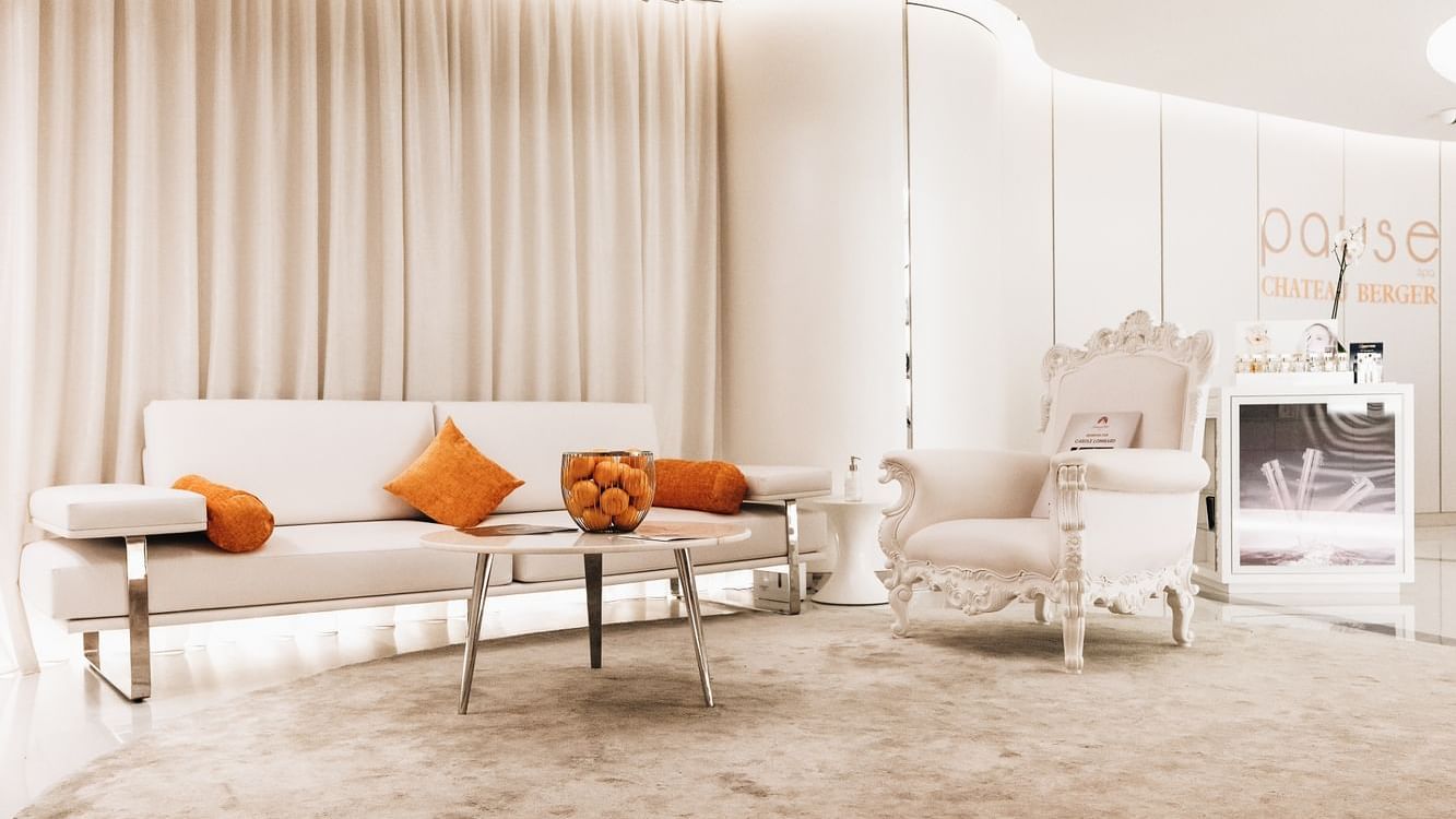 Stylish waiting room with a couch, ornate chair, & orange cushions in Pause Spa Chateau Berger at Paramount Hotel Dubai
