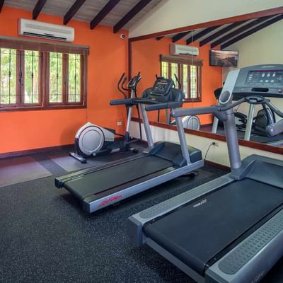 Treadmills and an elliptical trainer in a fitness center with vibrant orange walls at Sugar Cane Club Hotel & Spa