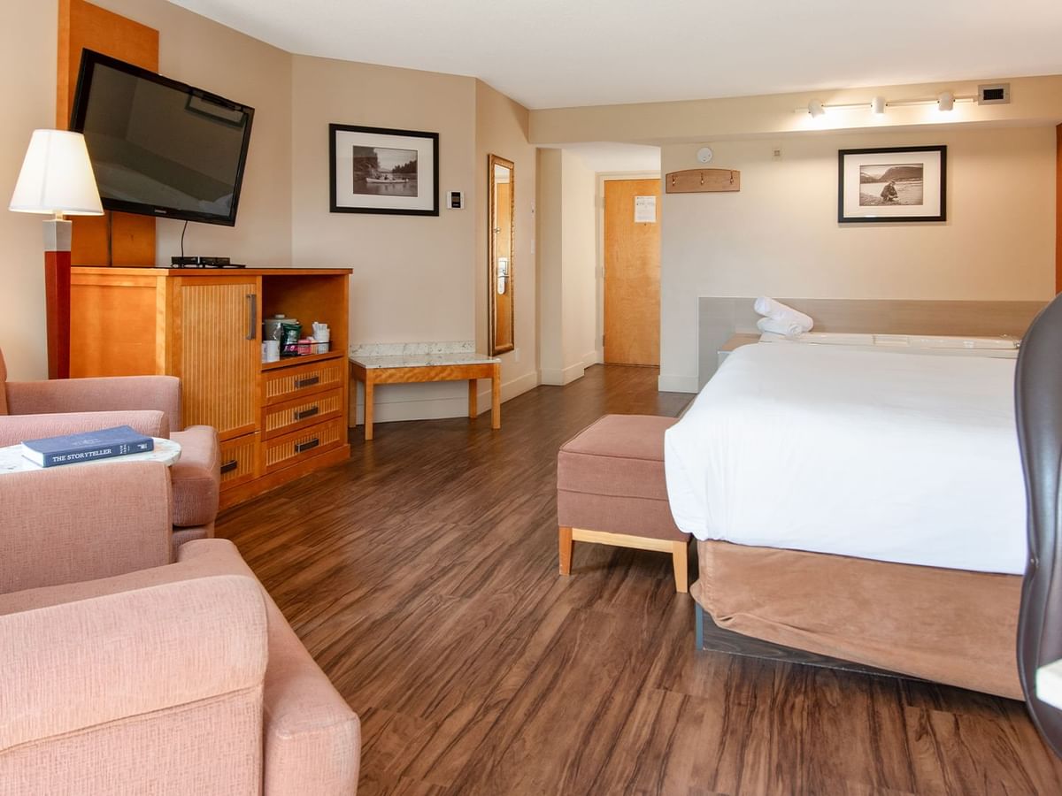 Hotel suite with king bed, TV, and arm chairs