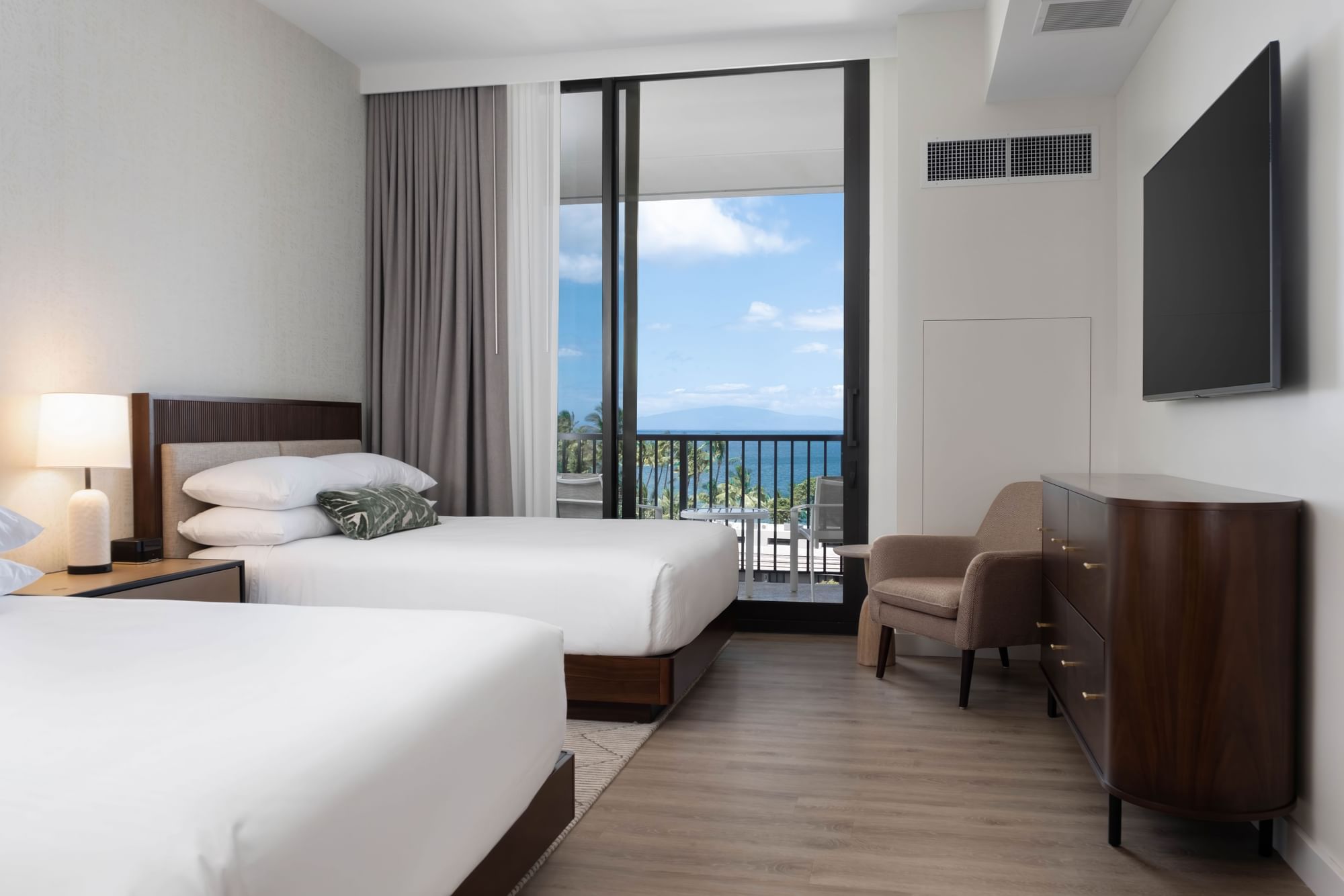 A hotel room with two double beds, a balcony, and a view of the ocean.