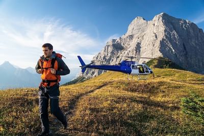 Hiker approaching a blue helicopter with a majestic mountain backdrop near Blackstone Mountain Lodge
