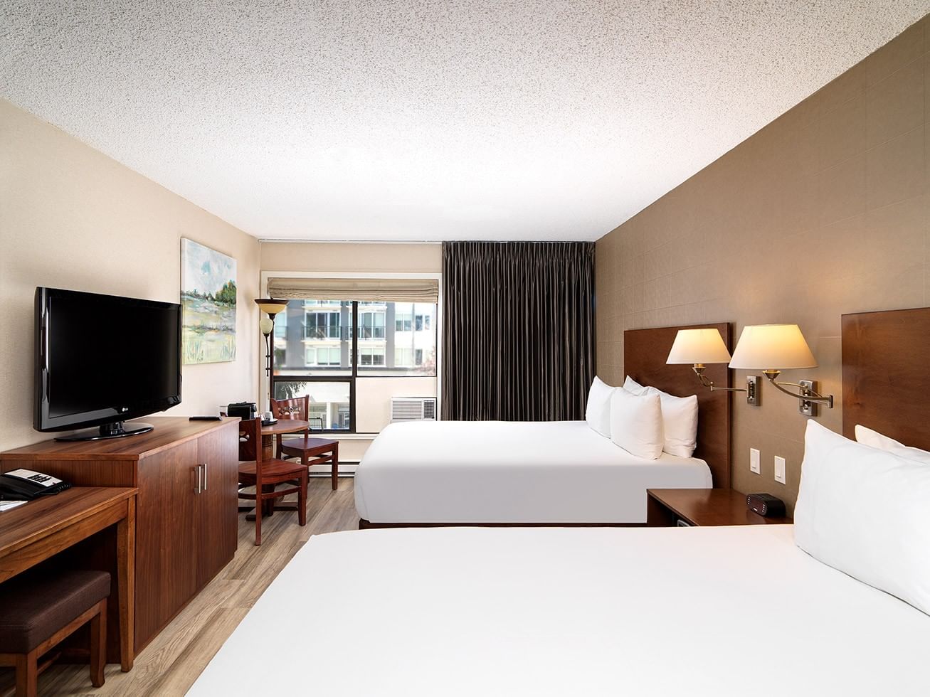 Hotel room with two beds, TV, desk, and a window with curtains and view of a building.