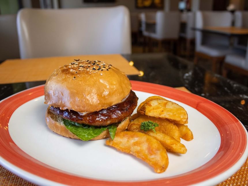 Hamburguesa gourmet con pan de sésamo y gajos de patata en un plato de Cafetería Palmira de Araiza Calafia
