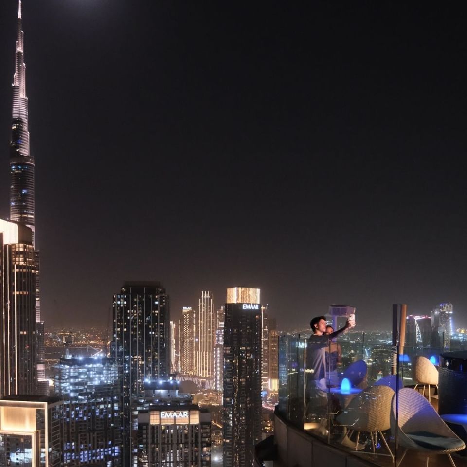 Couple taking a selfie on a high-rise balcony at night with the lit-up Burj Khalifa skyline from the Malibu Sky Lounge & Bar