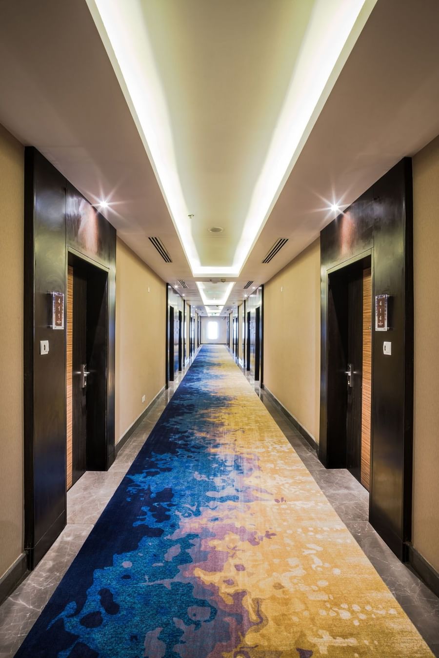 Hallway with a blue and yellow carpet lined with dark wood doors leading to the Junior Suite at Naviti by Warwick Dammam