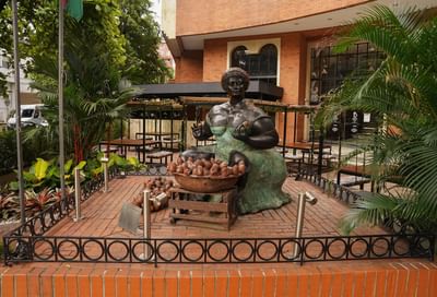 Statue of a seated woman in traditional attire, surrounded by plants and outdoor seating at Dann Carlton Cali