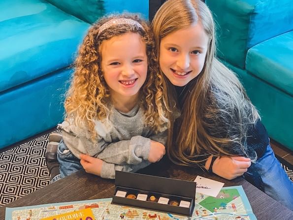 Due ragazze sorridenti sedute ad un tavolo con giochi e cioccolatini a DUPARC Contemporary Suites