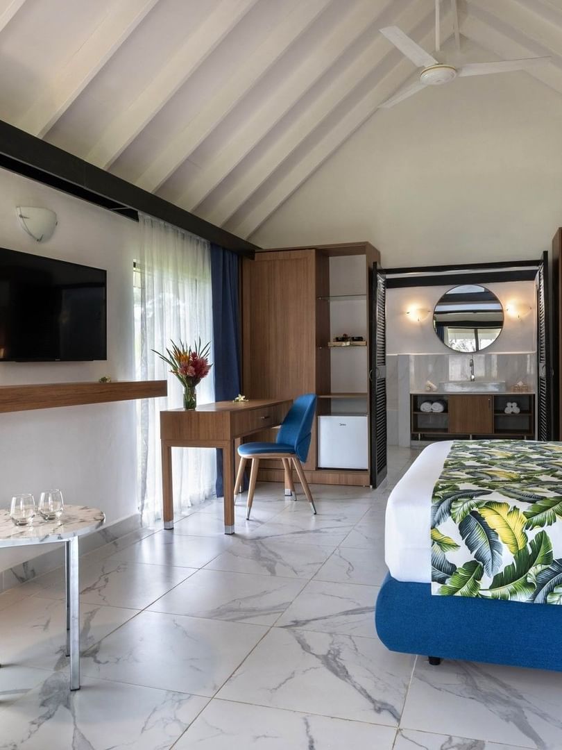 White bed with green lines facing wall mounted TV and beside seating area in Garden Bungalow at warwick le lagon-vanuatu