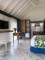 White bed with green lines facing wall mounted TV and beside seating area in Garden Bungalow at warwick le lagon-vanuatu