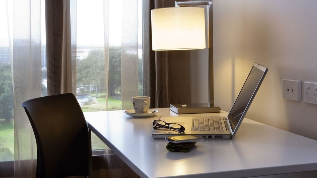 Brightly lit work desk with a laptop and coffee cup by window in the Superior Room at Novotel Sydney International Airport