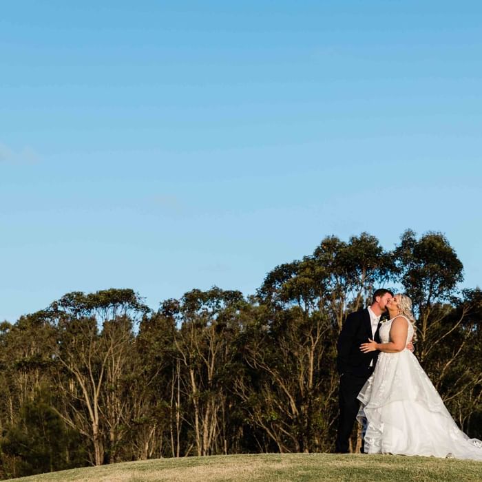 Bride and groom embrace outdoors with soft lighting in the background at Mercure Kooindah Waters
