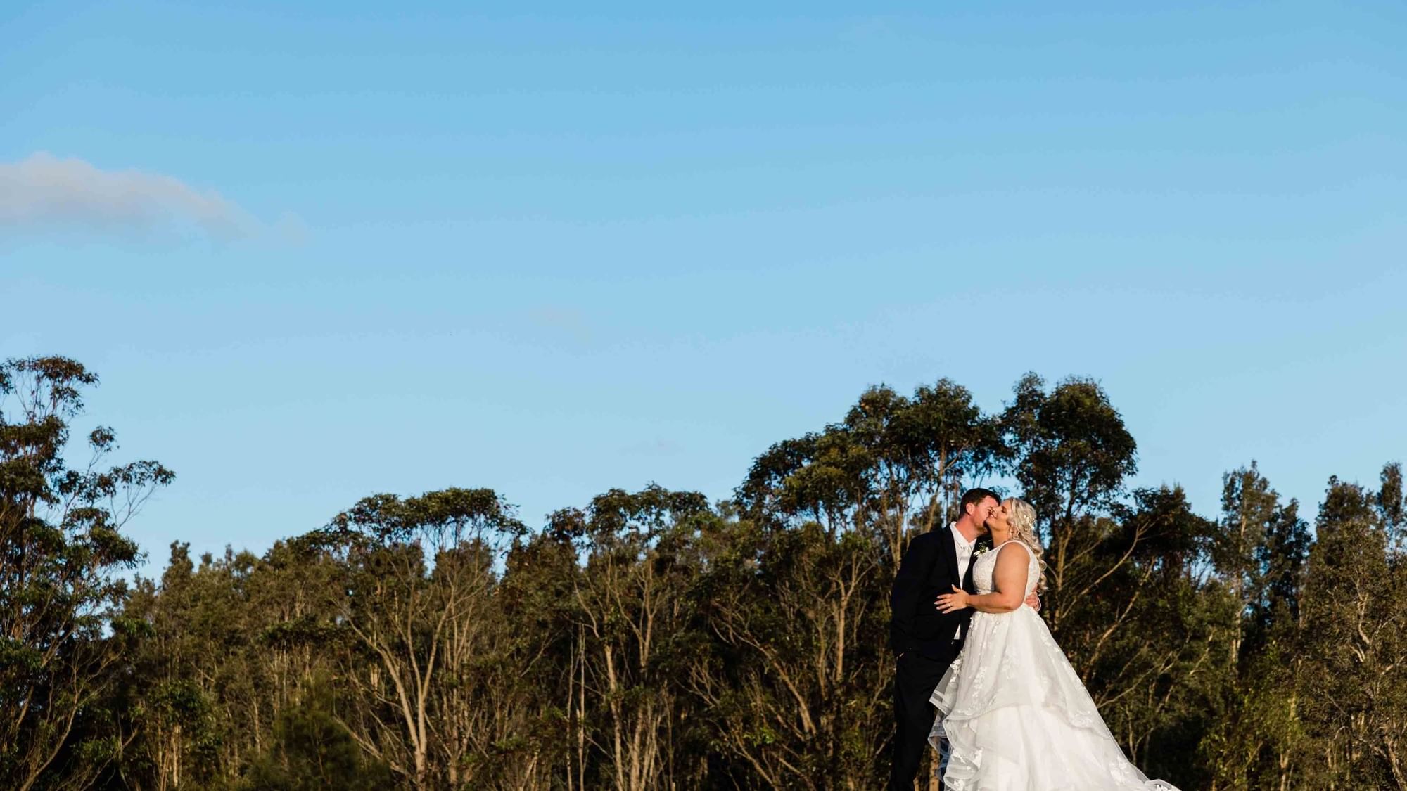 Bride and groom embrace outdoors with soft lighting in the background at Mercure Kooindah Waters