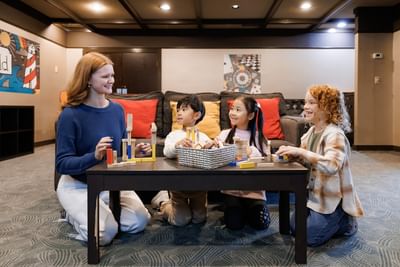 Adult woman with three young kids playing with building blocks around a dark coffee table at the Rodd Royalty
