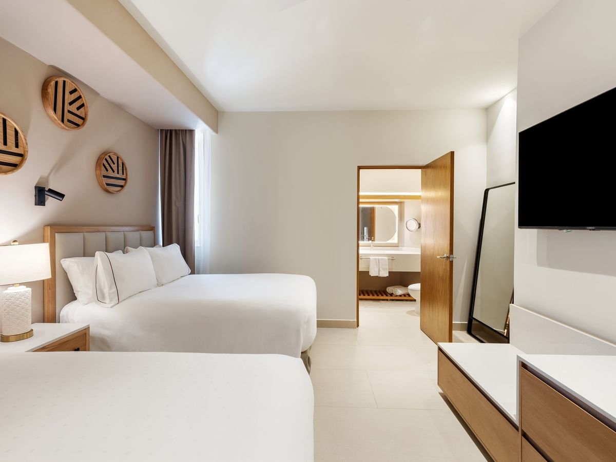 Suite De 2 Habitaciones Con Vista Frontal Al Mar with two beds, a TV, and an open bathroom door at Sunvivia Mazatlán