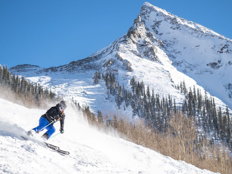 Skier in full gear skillfully navigating a snowy slope against a majestic mountain backdrop at Elevation Resort Spa