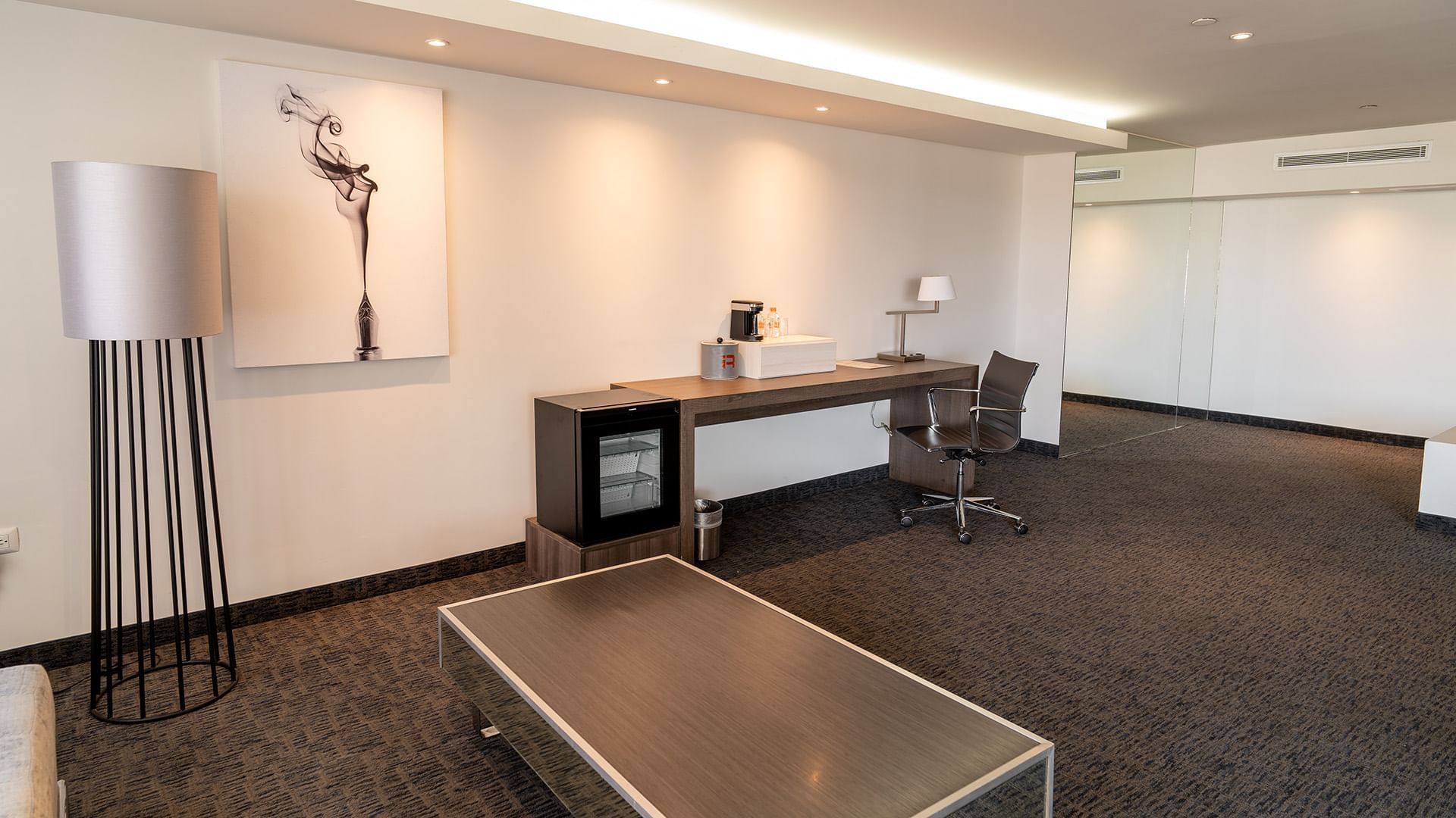 Workspace with coffee maker and modern wall art in the King Presidential Suite with carpeted floors at Real Inn Tijuana