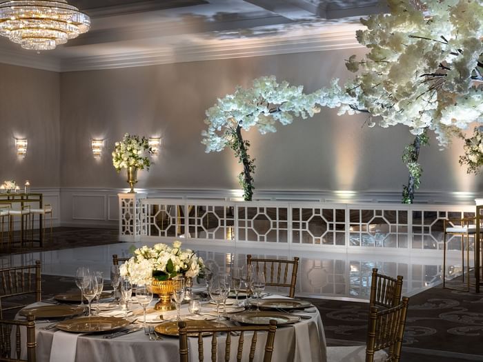 Round table by gold chairs under crystal chandeliers in Turtle Creek Ballroom C at Warwick Melrose Dallas